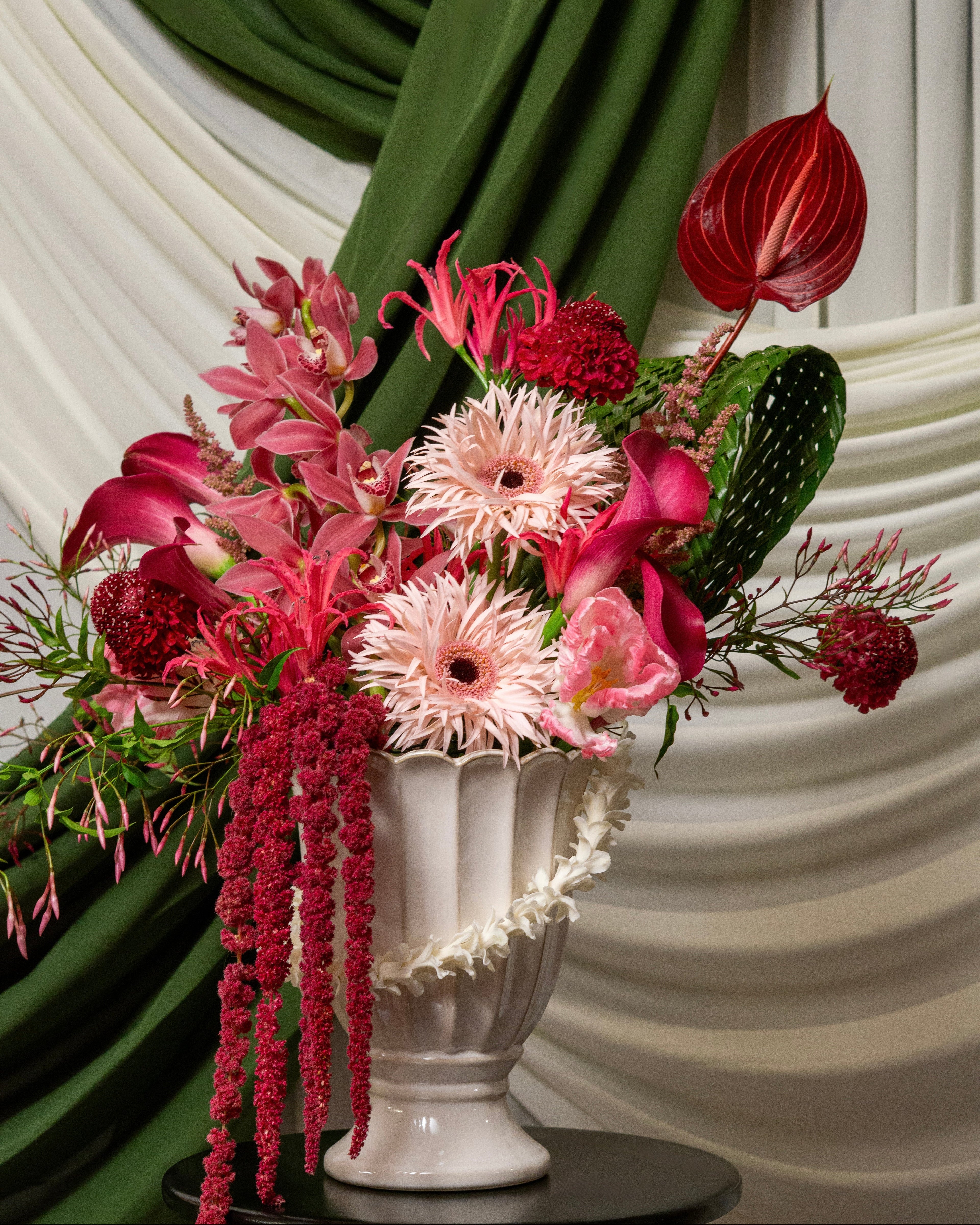 Floral arrangement in a white urn against a green and white draped background