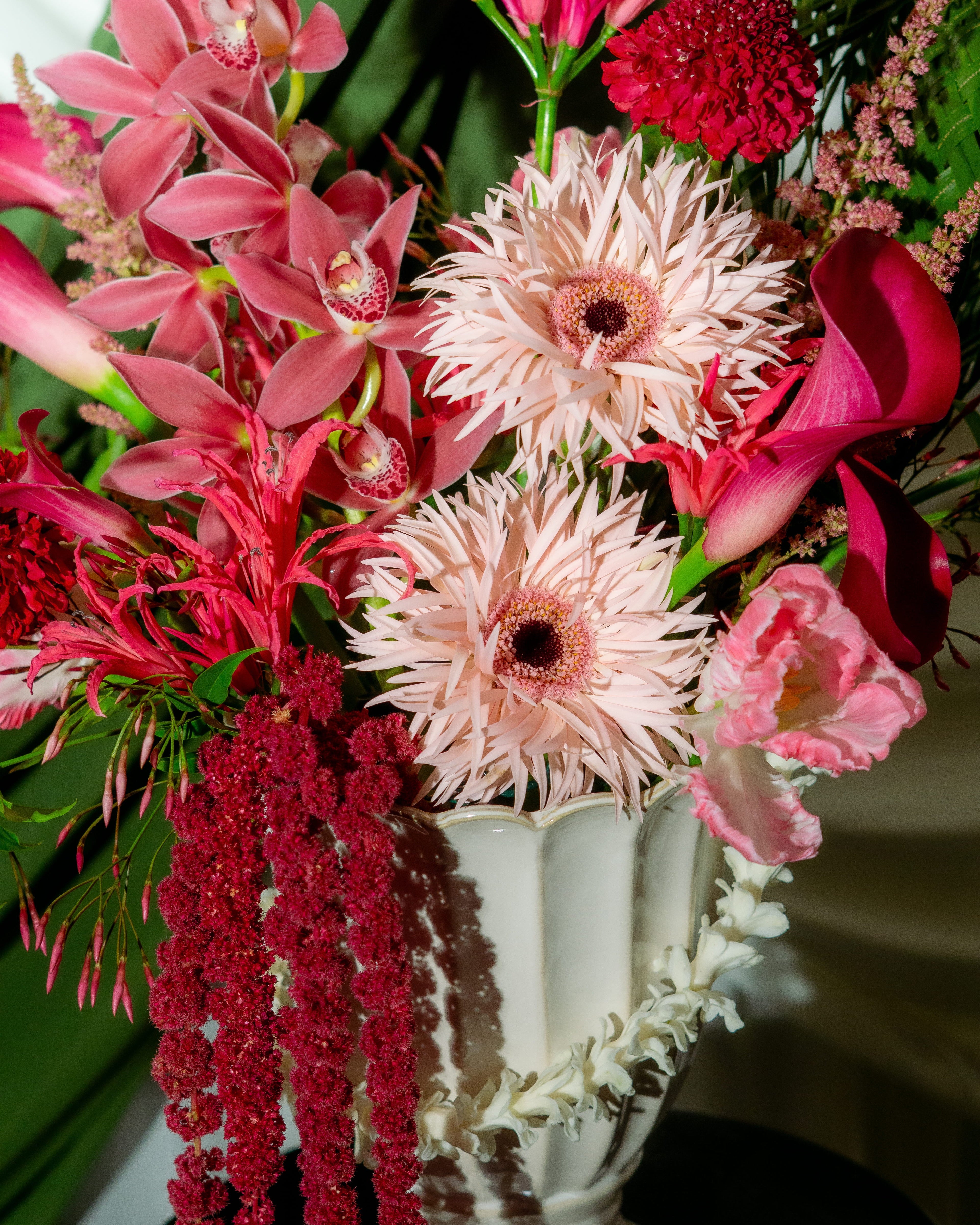 Bouquet of pink and red flowers in a white vase on a dark surface.