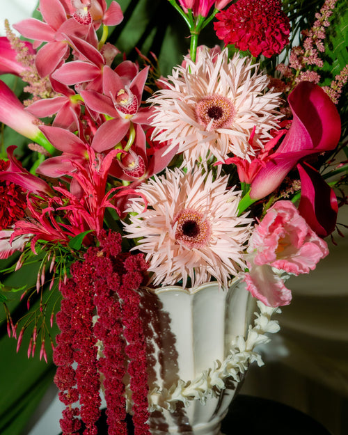 Bouquet of pink and red flowers in a white vase on a dark surface.